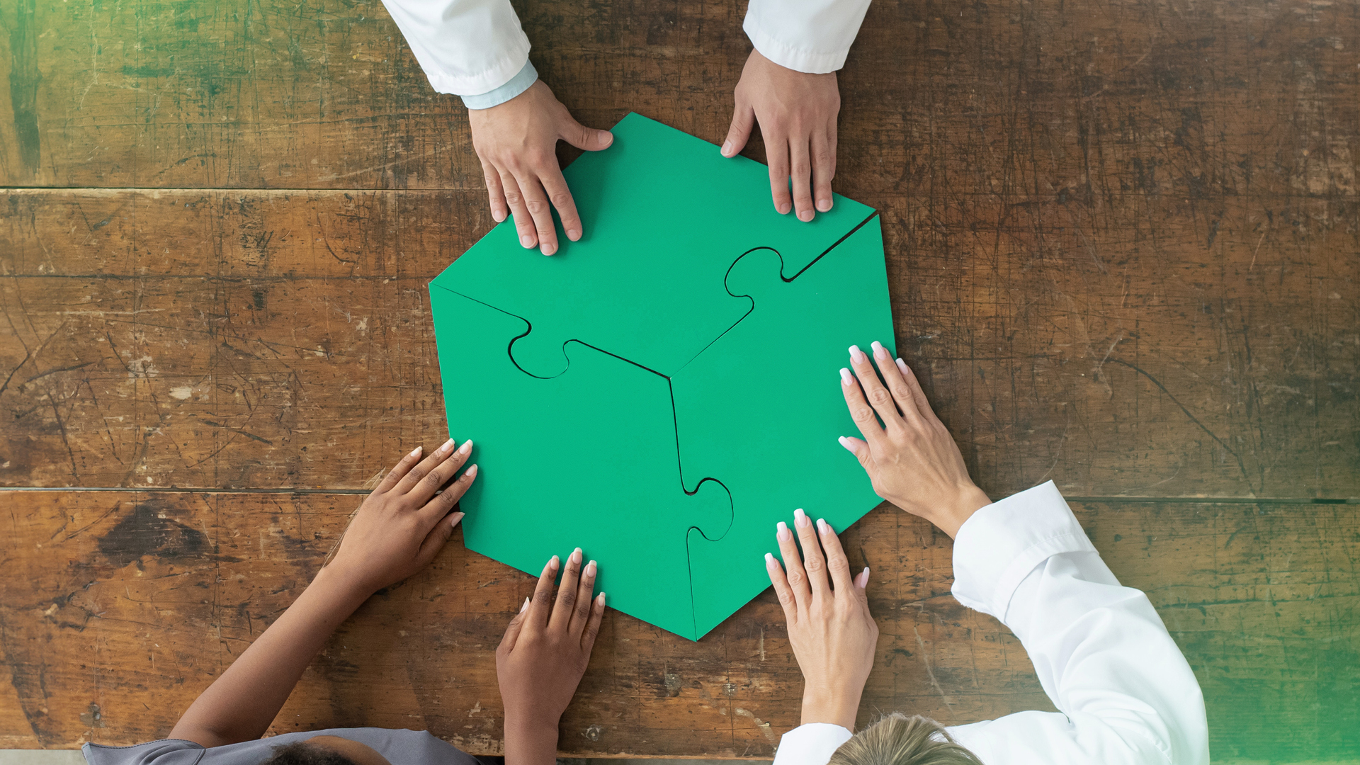 Drei Ärzt:innen halten jeweils ein grünes Stück eines Puzzles, welche Teil eins Hexagons sind.