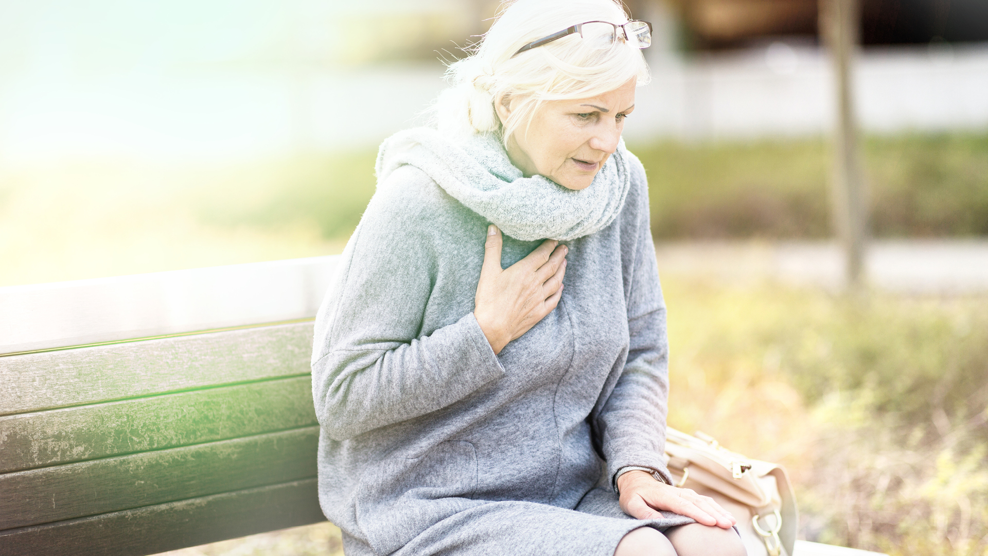 Frau auf Bank sitzend, Hand liegt auf Herz