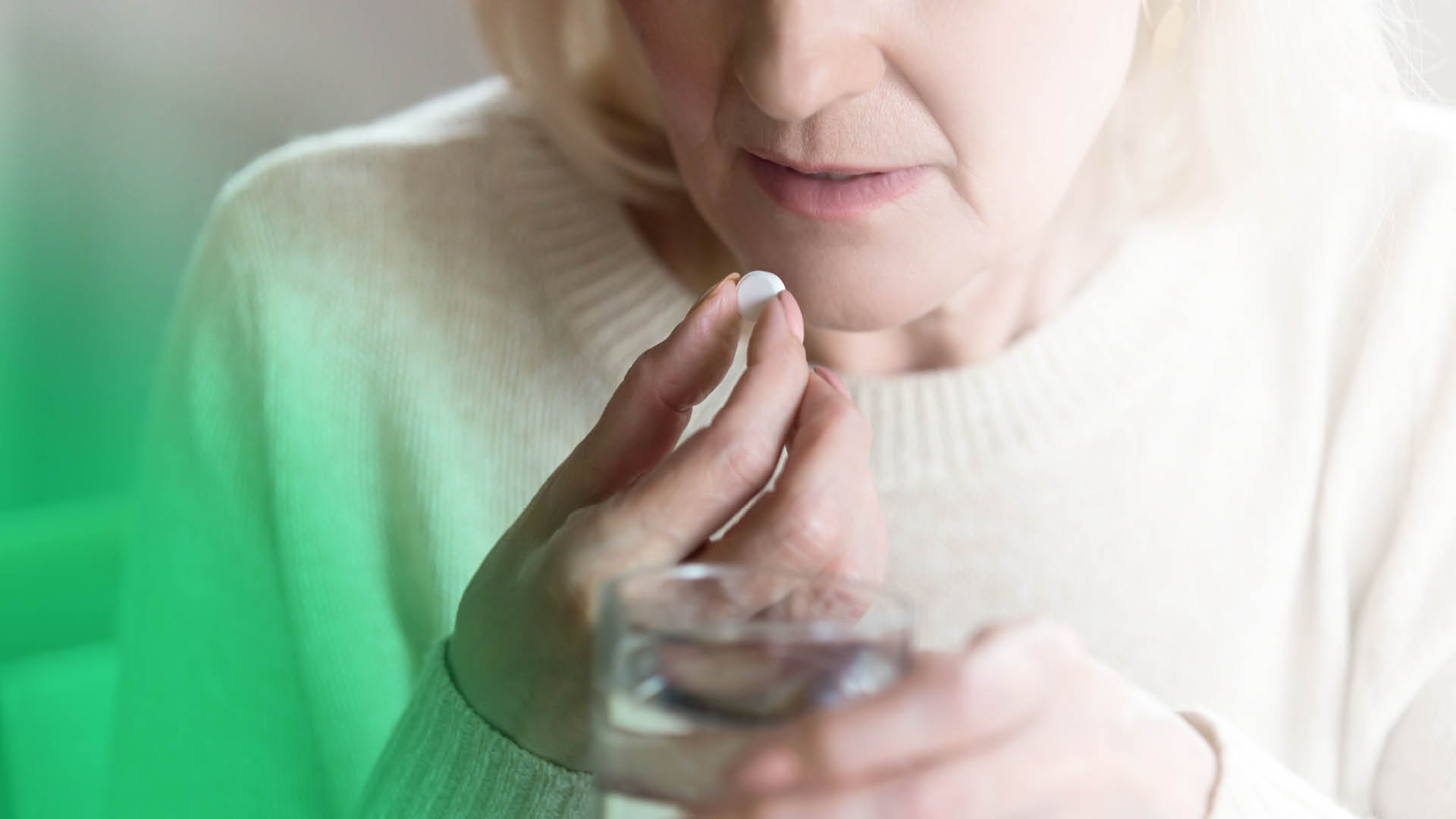 Ältere Frau nimmt Tablette mit einem Glas Wasser ein, Nahaufnahme der Hände, Symbolbild für SGLT2-Hemmer Einnahme ohne Altersbeschränkung bei Diabetes-Therapie.