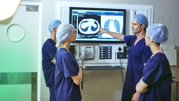 Vier Ärztinnen und Ärzte stehen vor einem Screen und schauen sich HRCT-Bilder an