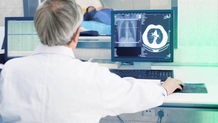 Ein Arzt sitzt mit dem Rücken zum Betrachter und schaut sich an einem Computer HRCT-Aufnahmen an