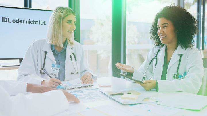 Zwei Ärztinnen im Gespräch in einer hellen Arztpraxis mit medizinischen Unterlagen auf dem Tisch