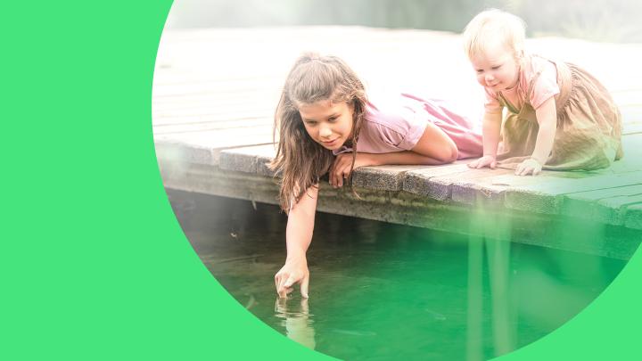 Zwei Kinder spielen am Steg und beugen sich über das Wasser.